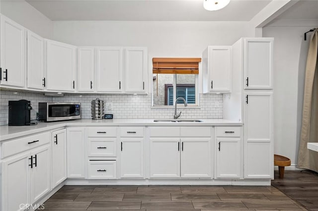 kitchen featuring stainless steel microwave, decorative backsplash, white cabinetry, and a sink