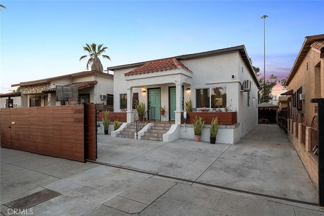 back of property at dusk with fence, a tile roof, and stucco siding