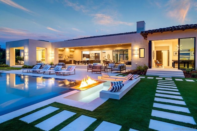 back house at dusk featuring a patio and an outdoor living space with a fire pit