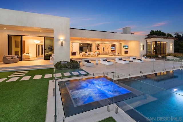 back house at dusk with a yard, a patio, and a pool with hot tub