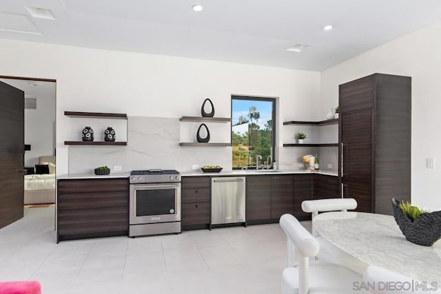 kitchen with appliances with stainless steel finishes, backsplash, dark brown cabinets, sink, and light tile patterned flooring