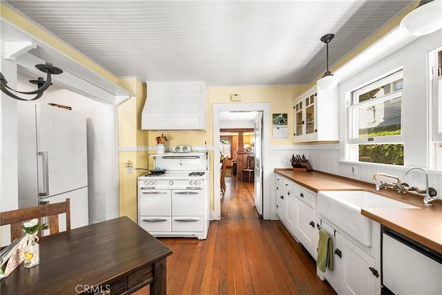 kitchen featuring custom range hood, white appliances, decorative light fixtures, dark hardwood / wood-style floors, and white cabinetry