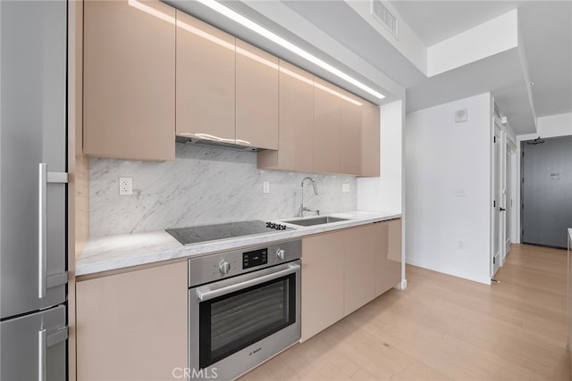 kitchen featuring tasteful backsplash, stainless steel appliances, sink, light hardwood / wood-style floors, and range hood