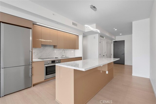 kitchen with appliances with stainless steel finishes, sink, backsplash, light hardwood / wood-style floors, and light stone countertops