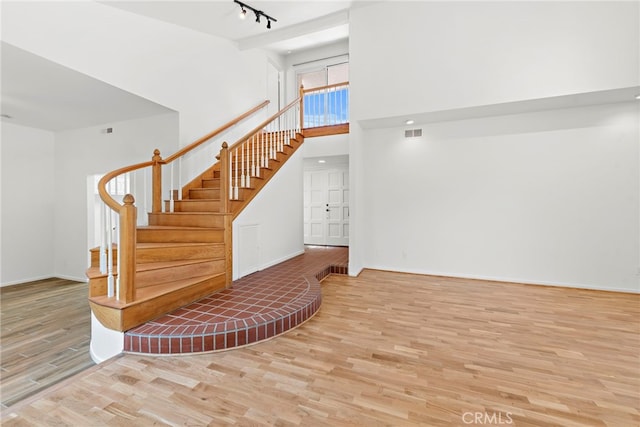 stairway featuring a towering ceiling, light hardwood / wood-style floors, and rail lighting