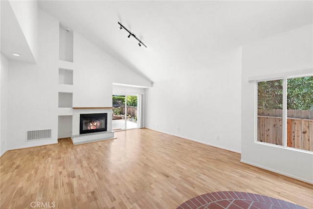 unfurnished living room with high vaulted ceiling, track lighting, and light wood-type flooring