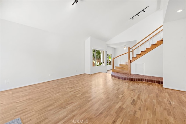 unfurnished living room featuring high vaulted ceiling, track lighting, and light hardwood / wood-style flooring