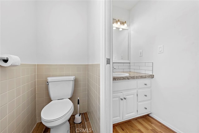 bathroom with wood-type flooring, vanity, toilet, and tile walls