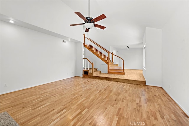 unfurnished living room with a high ceiling, ceiling fan, and light wood-type flooring