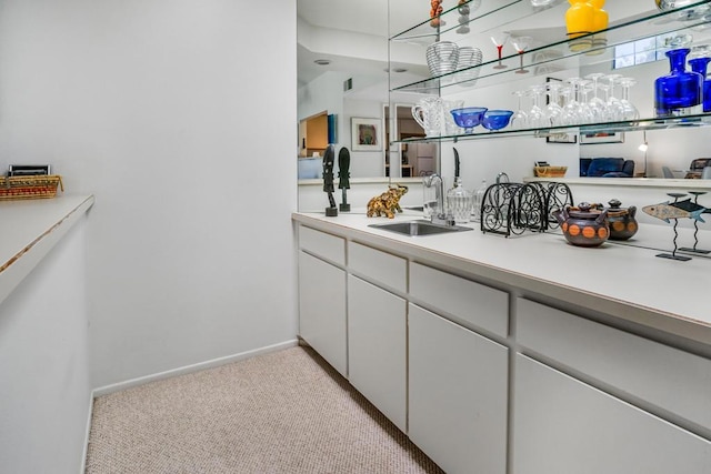 kitchen with white cabinetry, sink, and light carpet