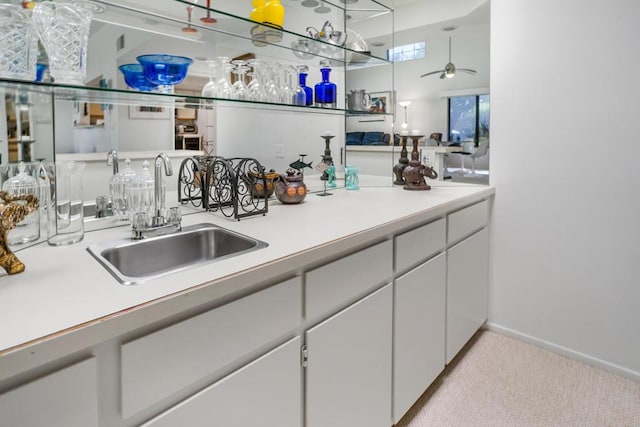 kitchen with white cabinets, ceiling fan, light colored carpet, and sink