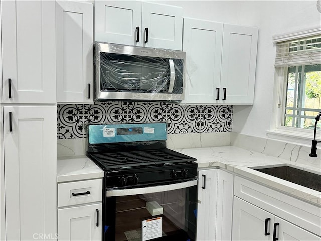 kitchen featuring sink, black range with gas stovetop, light stone counters, decorative backsplash, and white cabinets