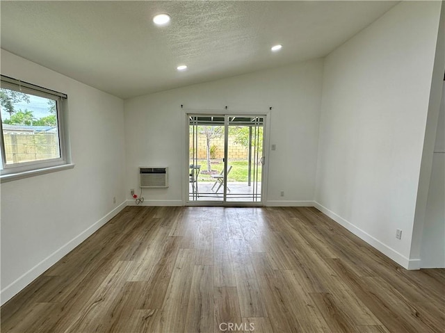 spare room with wood-type flooring, vaulted ceiling, a wealth of natural light, and a wall unit AC