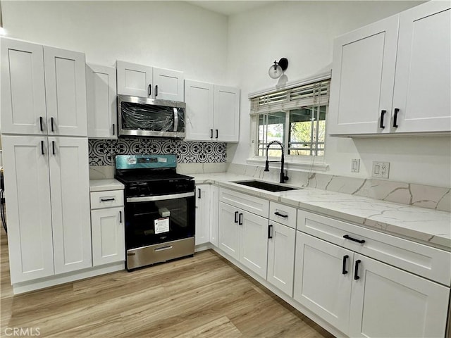 kitchen with light stone countertops, appliances with stainless steel finishes, light wood-type flooring, sink, and white cabinetry