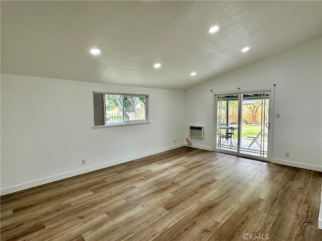 spare room with light hardwood / wood-style floors, a healthy amount of sunlight, a wall unit AC, and vaulted ceiling