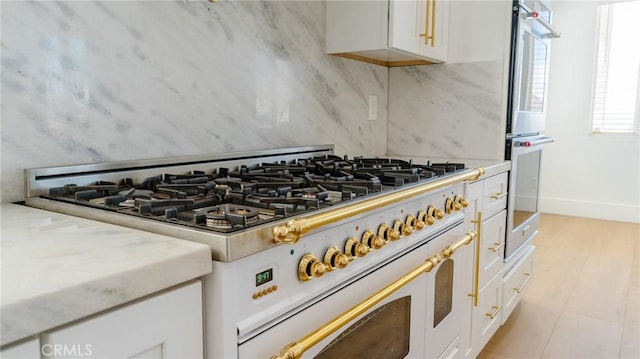 kitchen featuring tasteful backsplash, light stone counters, high end stove, double oven, and white cabinetry