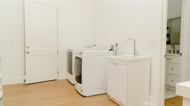 laundry area with sink, light hardwood / wood-style flooring, and washing machine and clothes dryer