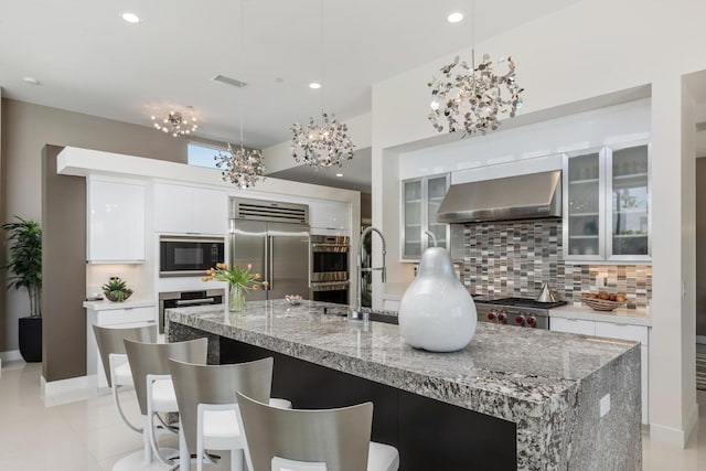 kitchen with pendant lighting, wall chimney exhaust hood, decorative backsplash, appliances with stainless steel finishes, and white cabinetry