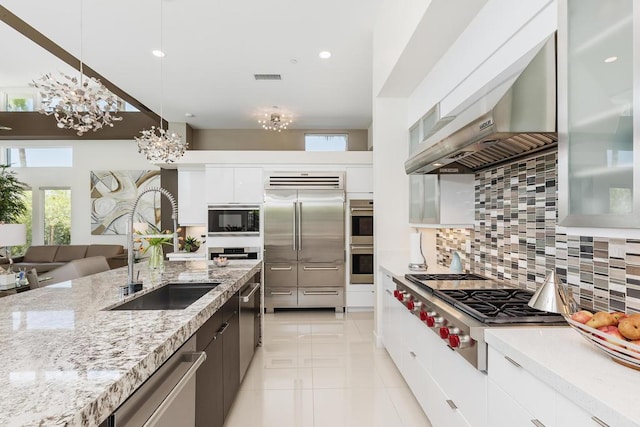 kitchen with decorative backsplash, sink, built in appliances, white cabinetry, and hanging light fixtures