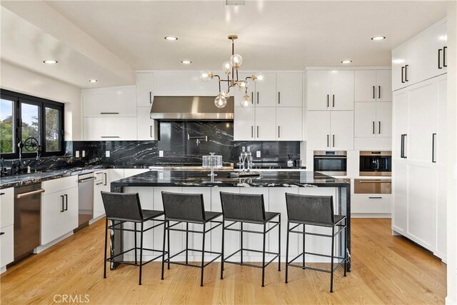 kitchen featuring appliances with stainless steel finishes, a kitchen island, wall chimney exhaust hood, and light hardwood / wood-style floors