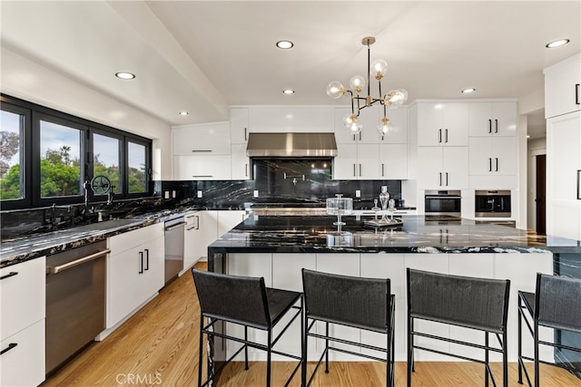 kitchen featuring decorative backsplash, white cabinetry, dishwasher, wall chimney exhaust hood, and light hardwood / wood-style floors