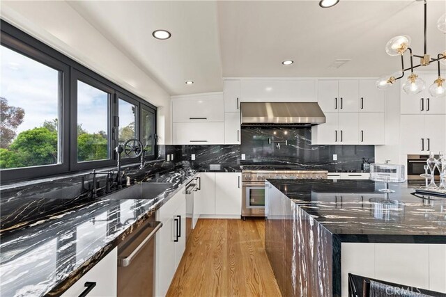 kitchen featuring pendant lighting, decorative backsplash, dark stone counters, light hardwood / wood-style flooring, and wall chimney range hood