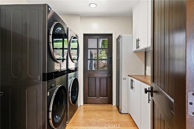 laundry room featuring cabinets, stacked washer and dryer, and light hardwood / wood-style floors