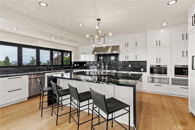 kitchen with appliances with stainless steel finishes, a kitchen island, tasteful backsplash, light hardwood / wood-style floors, and wall chimney exhaust hood