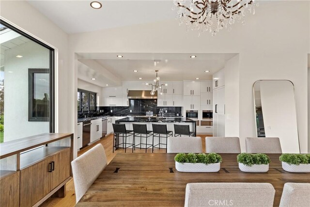 dining area featuring vaulted ceiling, light hardwood / wood-style floors, and an inviting chandelier