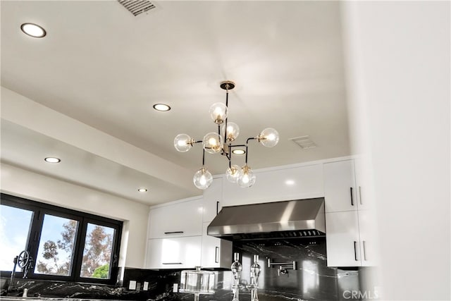 details featuring decorative light fixtures, wall chimney range hood, a chandelier, and white cabinetry