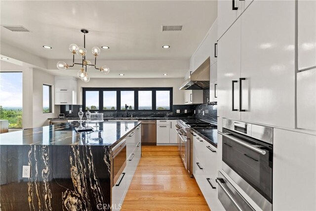 kitchen featuring wall chimney exhaust hood, white cabinets, a wealth of natural light, and light hardwood / wood-style floors