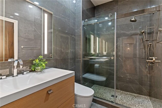 bathroom featuring tile walls, a shower with door, toilet, and vanity