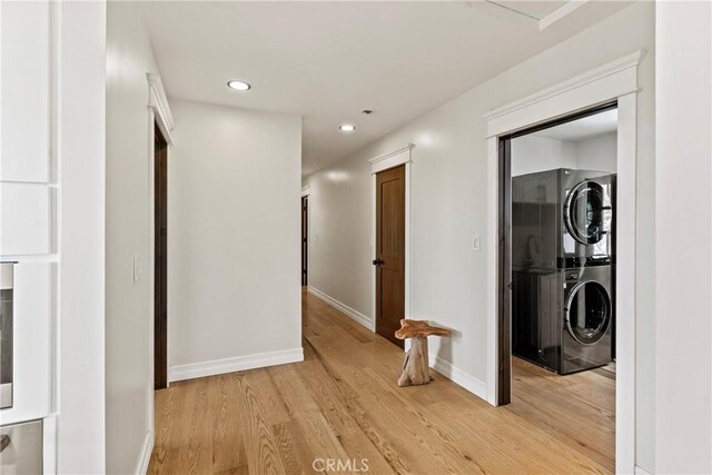 hall with light wood-type flooring and stacked washing maching and dryer