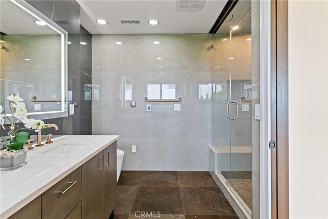 bathroom featuring a shower with shower door, vanity, tile walls, and tile patterned floors