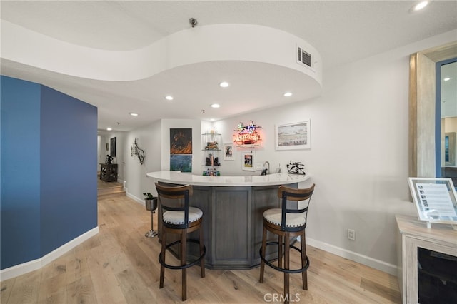 bar featuring light wood-type flooring, visible vents, wet bar, and baseboards