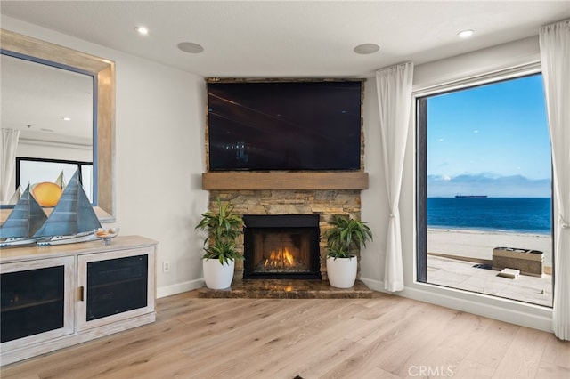 living area featuring recessed lighting, a stone fireplace, light wood-style flooring, and baseboards