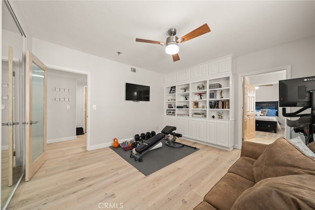 exercise room with visible vents, baseboards, a ceiling fan, light wood-style floors, and built in shelves