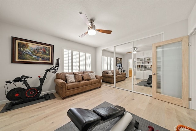 exercise area featuring light wood-style floors, ceiling fan, a textured ceiling, and baseboards