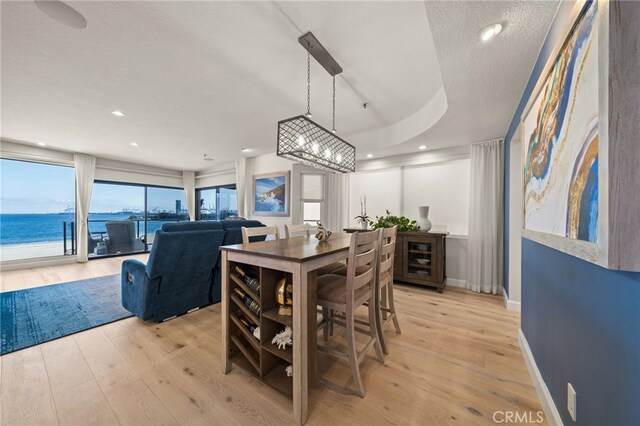 dining space featuring a raised ceiling, a water view, light wood-type flooring, and a textured ceiling