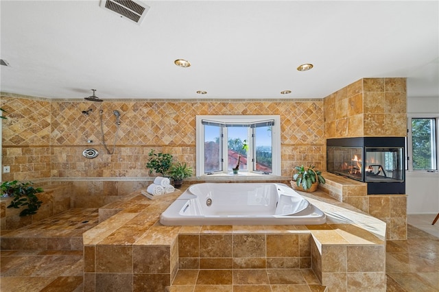 bathroom with plus walk in shower, ceiling fan, a healthy amount of sunlight, and a fireplace