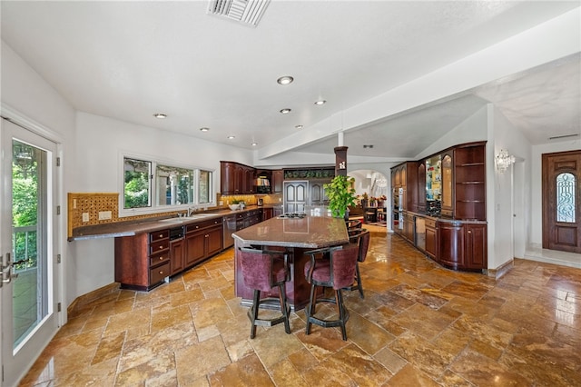 kitchen featuring a center island with sink, decorative backsplash, dark brown cabinets, a breakfast bar, and sink