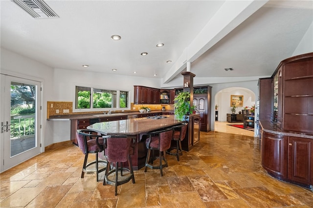 kitchen with dark stone countertops, a kitchen island, a breakfast bar, decorative backsplash, and sink