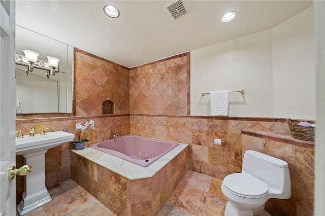 bathroom with a relaxing tiled tub, tile walls, toilet, and sink