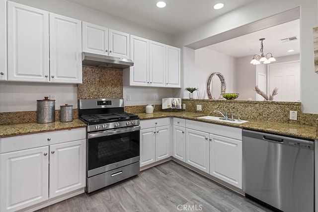 kitchen with stainless steel appliances, sink, light hardwood / wood-style floors, dark stone countertops, and white cabinetry