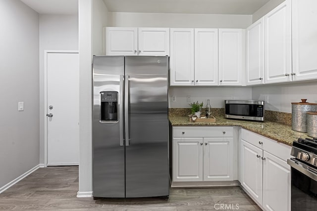 kitchen with dark stone counters, white cabinetry, light wood-type flooring, and stainless steel appliances