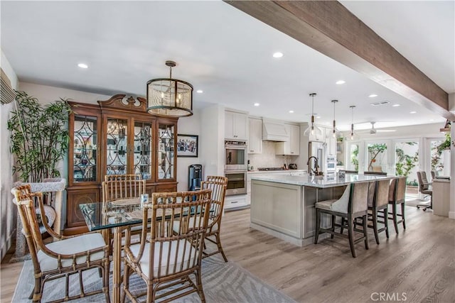 kitchen featuring a large island with sink, light wood-type flooring, white cabinetry, and hanging light fixtures