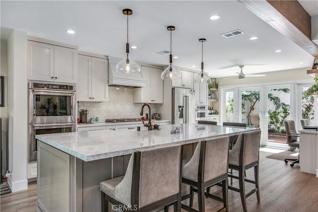 kitchen featuring decorative light fixtures, light hardwood / wood-style floors, light stone counters, and a large island