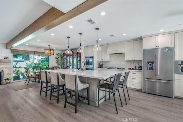 kitchen with beam ceiling, stainless steel appliances, a spacious island, decorative light fixtures, and custom range hood