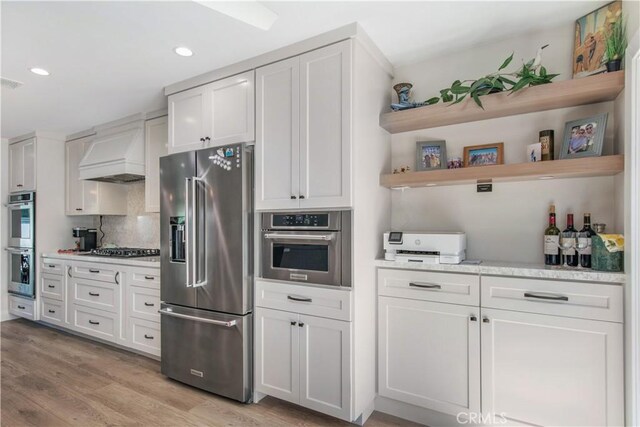 kitchen with white cabinets, light wood-type flooring, stainless steel appliances, and premium range hood