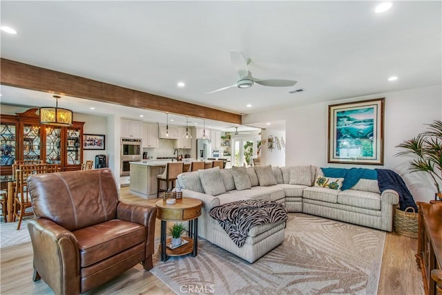 living room with ceiling fan, beam ceiling, and light wood-type flooring